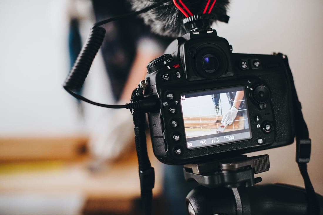 Caméra sur trépied équipée d’un micro, filmant un artisan au travail pendant un tournage vidéo