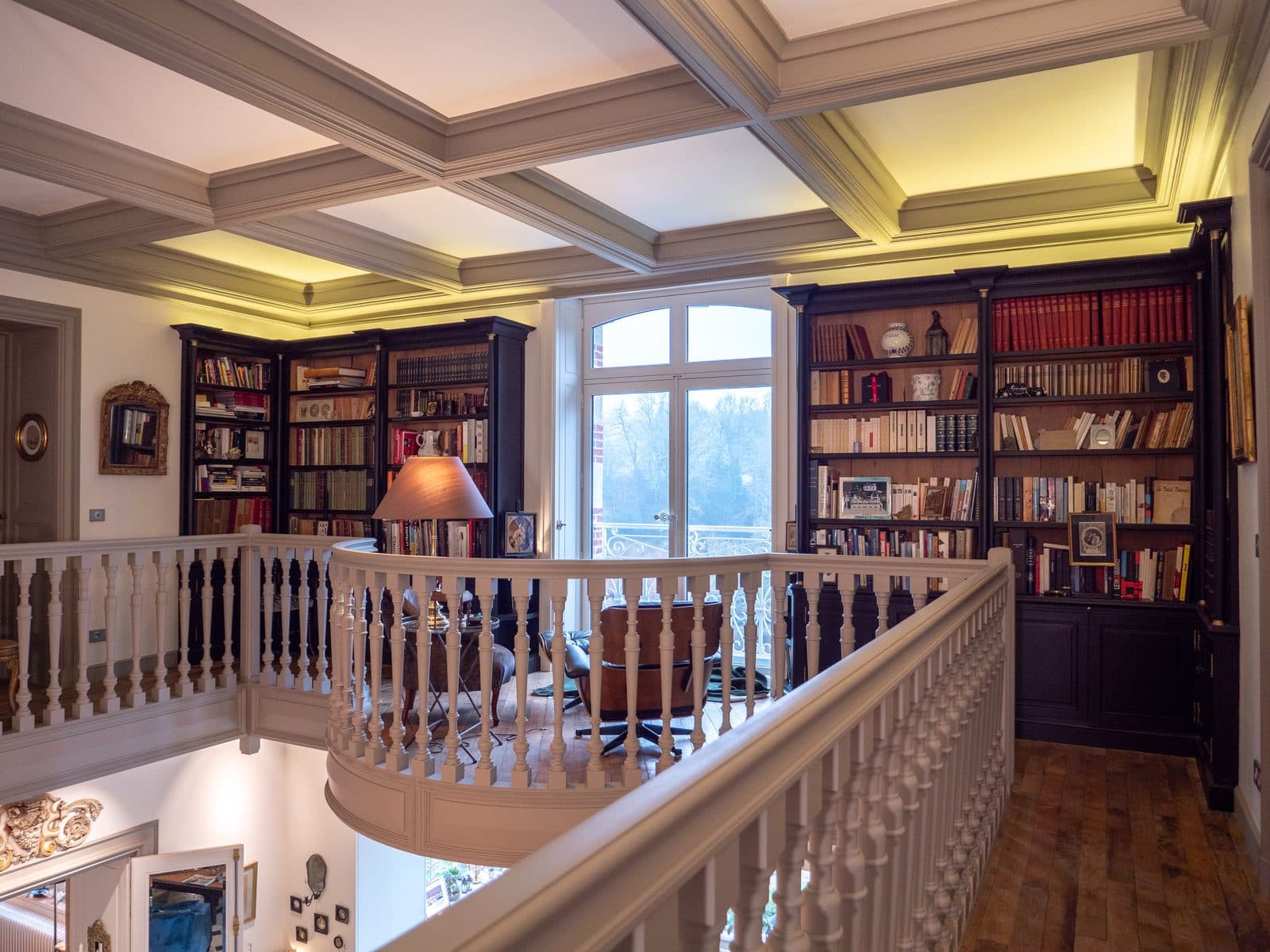 Mezzanine bordée de bibliothèques sous un plafond à caissons éclairé