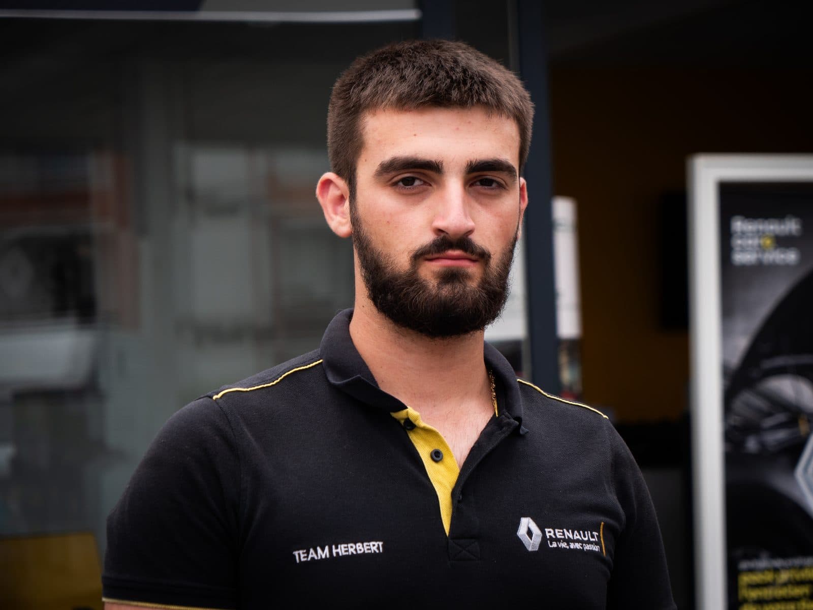 Portrait serré d’un jeune technicien devant la vitrine de la concession