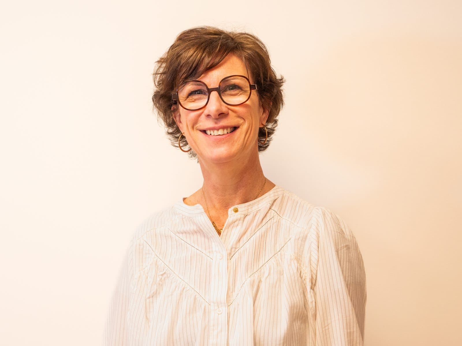 Portrait d’une collaboratrice souriante à lunettes sur fond clair
