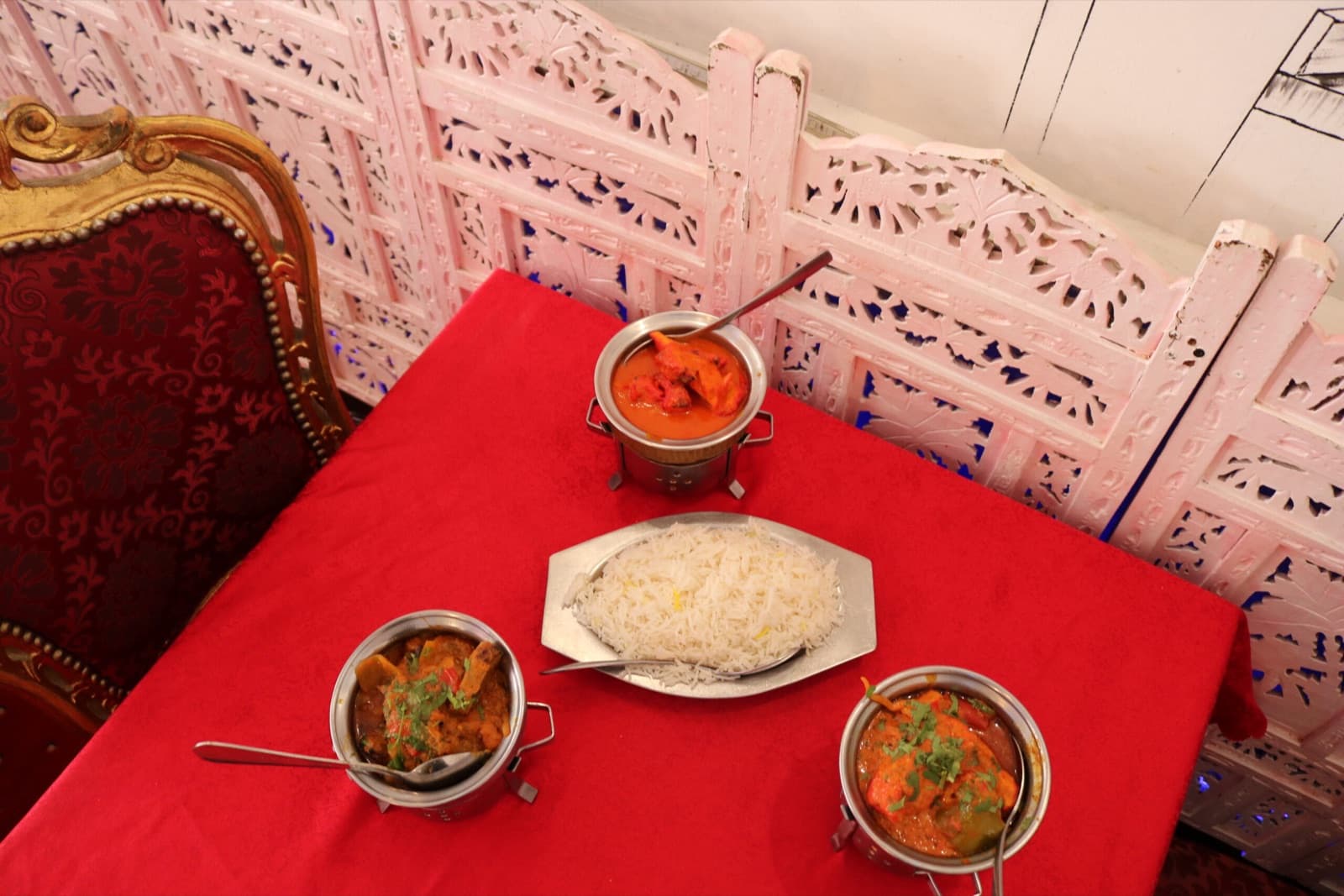 Plats indiens servis sur une nappe rouge devant un paravent sculpté